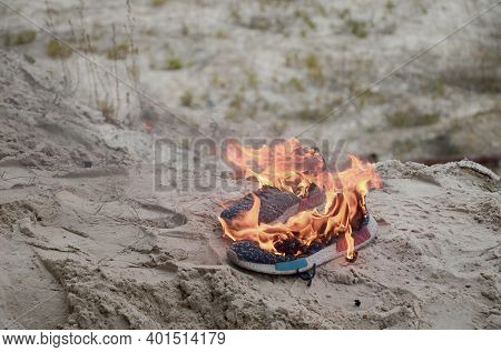 Burning Sports Sneakers Or Gym Shoes On Fire Stand On Sandy Beach Coast Close Up. Athlete Burned Out