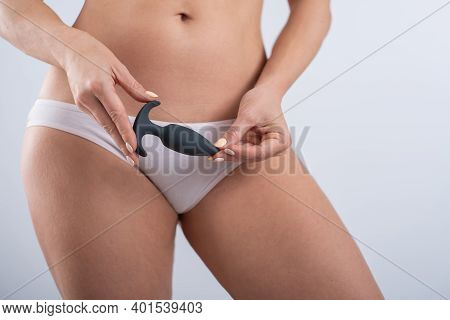 A Faceless Woman In White Cotton Panties Holds A Black Butt Plug On A White Background