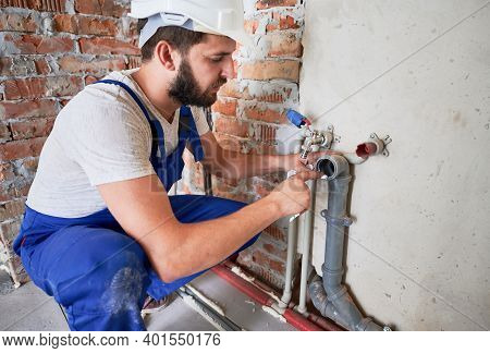 Young Plumber, Wearing Blue Uniform And White Helmet Working With Sealant Fix Of Sewer Pipe In Kitch