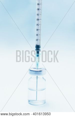 Punctured Syringe In A Bottle To Put A Vaccine On Blue Background.