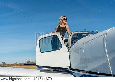A gorgeous young blonde model poses outdoors with a single engine aircraft at a local airport