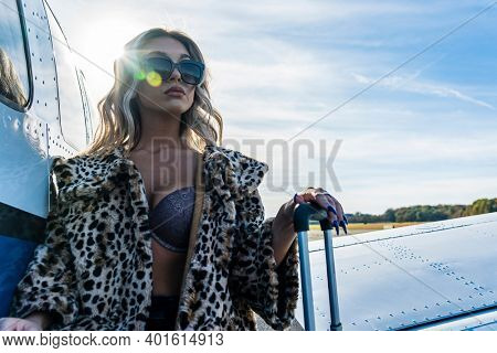 A gorgeous young blonde model poses outdoors with a single engine aircraft at a local airport