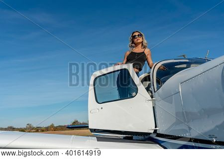 A gorgeous young blonde model poses outdoors with a single engine aircraft at a local airport