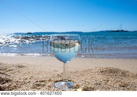 Glass Of Local Dry White Wine On White Sandy Beach And Blue Mediterranean Sea On Background, Near Le