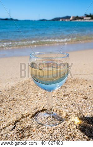 Glass Of Local Dry White Wine On White Sandy Beach And Blue Mediterranean Sea On Background, Near Le