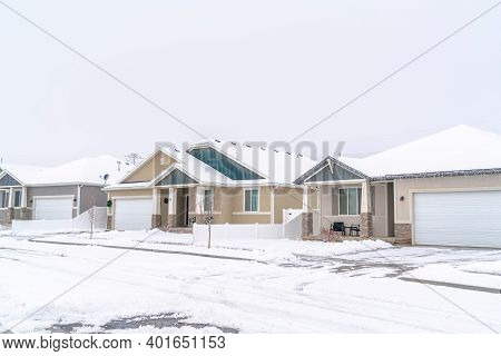 Front View Of Single Storey Family Homes With Attached Garages Against White Sky