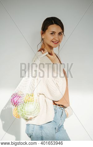 Sideways Portrait Of A Woman Posing In A Room, Holding Net Bag With Vegetables