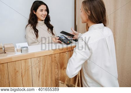 Happy Female Customer Making A Purchaise, Paying With Her Phone.