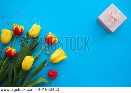 Bouquet Of Yellow And Red Tulips And A Pink Box With A Gift On A Blue Background. International Wome