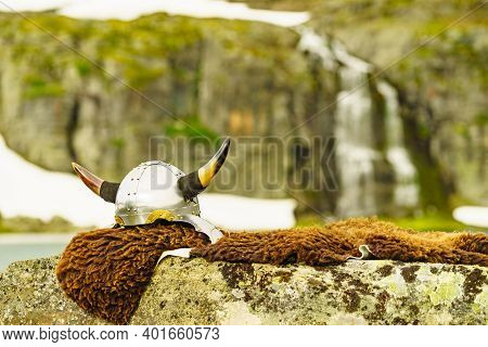 Equipment Of Viking Or Barbarian Warrior Outdoor On Nature. Viking Helmet On Brown Fur Of Animal In 