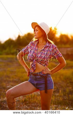 Amerikansk ung kvinde i Plaid Shirt og Denim Shorts, Hat ved solnedgang ser på afstand