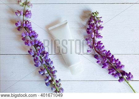 Mockup Of Unbranded White Bottle Tube For Branding And Purple Flowers On White Wooden Table With Hor