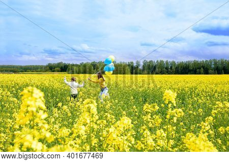 Yellow Field, Blue Sky, White Clouds. Running Cute Kids Kids With Blue And Yellow Balloons. The Conc