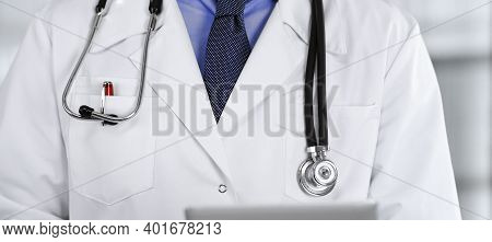 Unknown Male Doctor Iusing Tablet Computer In His Hands, While Standing In Clinic. Medicine Concept 