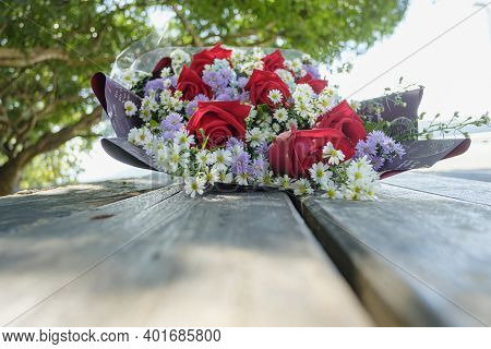 Close Up Of Red Roses In A Bouquet That Has White Cutters And Purple Daisy Included. On Floor Wooden