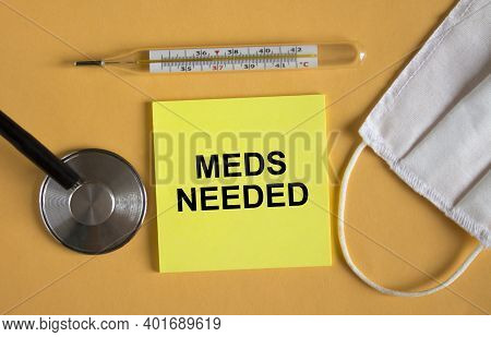 Sticker With Text Meeds Needed Lying On The Orange Background With Mask And Thermometer. Medical Con