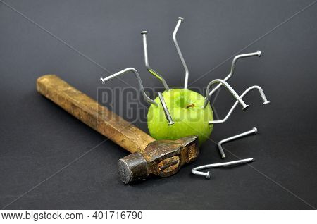Green Apple Pierced With Nails.an Old Wooden Hammer.