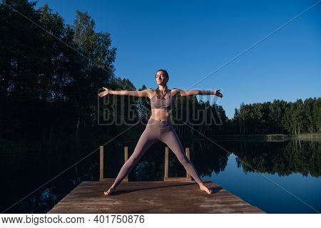 Young Woman Relaxing By The Lake At Sunset, Harms Outstretched. Doing Youga In The Morning At Forest