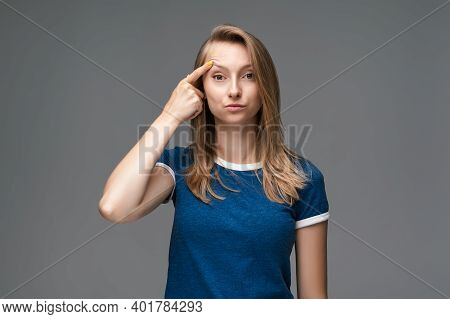 Young Female With Blonde Straight Hair And Wears Blue T Shirt Having Doubts Looks At The Camera, Her