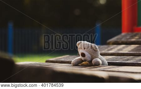 Lost Teddy Bear Lying On Wooden Bridge At Playground In Gloomy Day, Lonely And Sad Face Brown Bear D