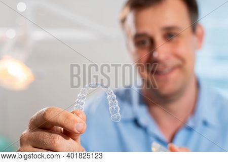 A Smiling Dentist Doctor Holds Transparent Aligners In His Hands