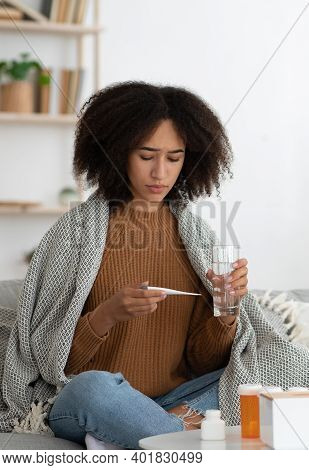 Health Problems, Cold, Flu And Covid-19. Sad Millennial African American Woman In Blanket Hold Glass