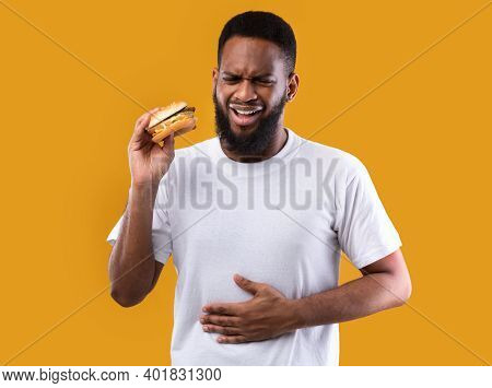 Unhealthy Eating. Black Man Suffering From Stomachache After Burger Touching Aching Stomach Standing