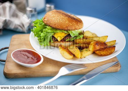 Homemade Burger With Potatoes And Salad On A Plate. Food On The Table In A White Plate On A Wooden B