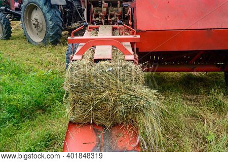 The Process Of Harvesting Hay For Cattle, A Tractor Making Bales In The Field, Old Machinery.