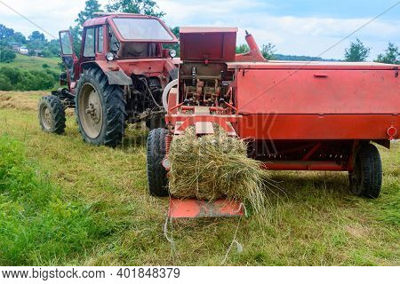 The Process Of Harvesting Hay For Cattle, A Tractor Making Bales In The Field, Old Machinery.