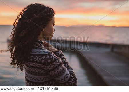 Young African American Woman Is Standing On The Promenade At The Lake, Looking Thoughtfully Towards 