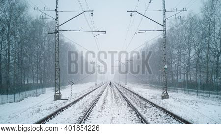 A Woman Walks Across Rail Train Tracks From One Side To Another Side On A Snowy Winter Day. The Dang