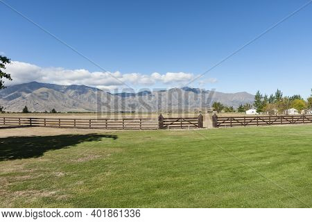 Post And Rail Fence Across Green Land With Distant Mountains.
