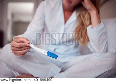 Close Up Of Unhappy Woman Wearing Pyjamas In Bedroom Holding Pregnancy Test