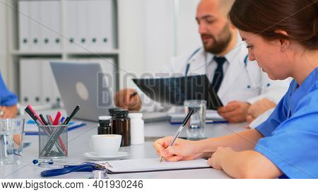 Close Up Of Nurse Taking Notes On Clipboard While Radiologist Coworkers Discussing In Background Ana