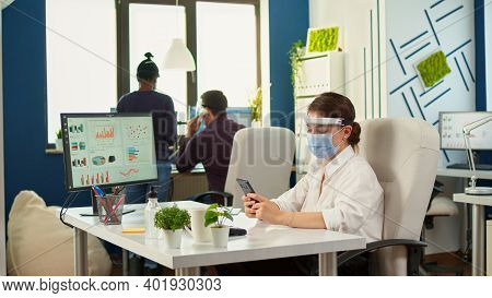 Businesswoman Chatting Using Phone In Office Room Sitting At Desk Wearing Face Mask And Visor While 