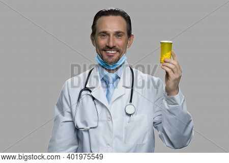 Happy Mature Doctor Showing Bottle Of Pills. Smiling Male Physician Holding Jar With Pills Against G