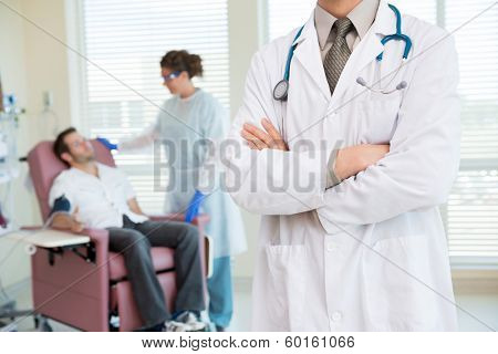 Midsection of male doctor standing arms crossed with nurse looking at patient being examined by pulse rate machine in hospital