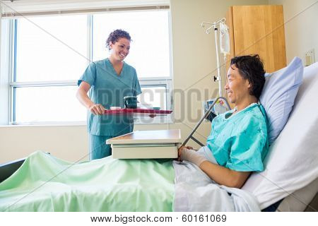 Happy mid adult nurse bringing breakfast for mature patient in hospital