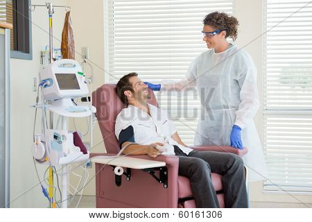 Female nurse looking at male chemo patient being monitored by heartbeat machine in hospital