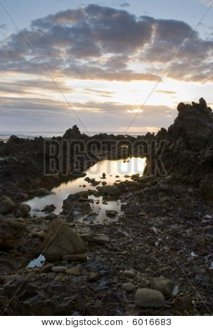 岩の多いビーチに曇り沈む夕日