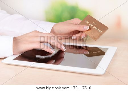 Female hands holding credit card and computer tablet on table on bright background