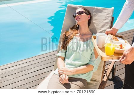 Asleep young woman and cropped waiter with breakfast tray by the pool