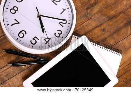 Tablet, cup of coffee, notebook and clock on wooden background