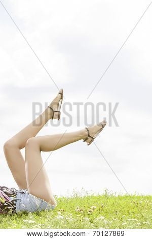 Low section of woman with feet up lying on grass against sky