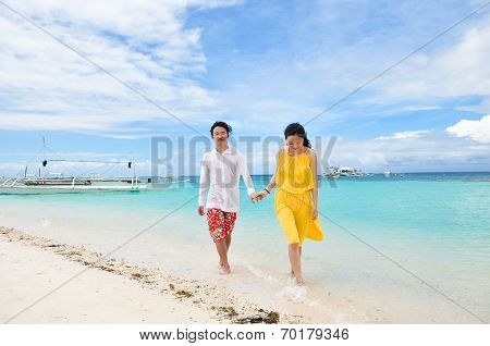 happy young couple walks in shallow water on tropical beach
