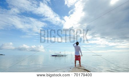 standing young man looks at horizon on beach