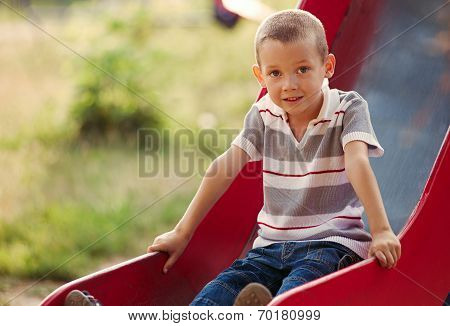 Small Boy Playing On A Slide In A Kids Playground