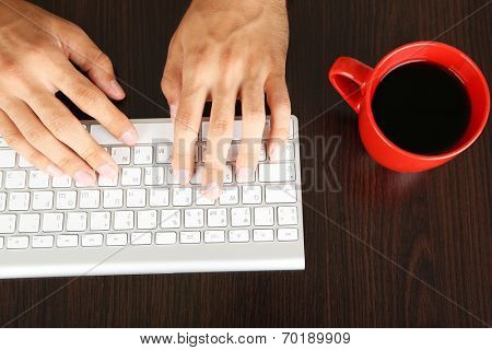 Man working with keyboard on wooden table on folders background closeup