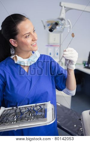 Smiling dentist holding tray and looking angle mirror in dental clinic